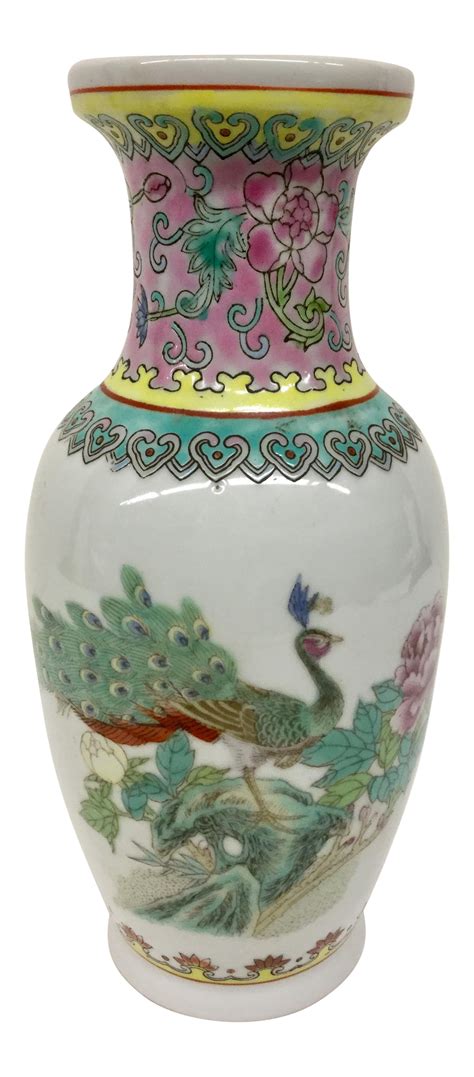 The vase depicts a pair of peacocks with wings in closed position, the male's plumage displayed in brilliant blues and greens. Coral and pink flowers, along with green and blue-hued foliage fill the remaining landscape of the vase.